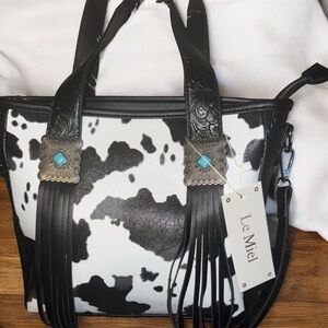 This is a Le Miel black and white cow print tote/crossbody bag featuring western